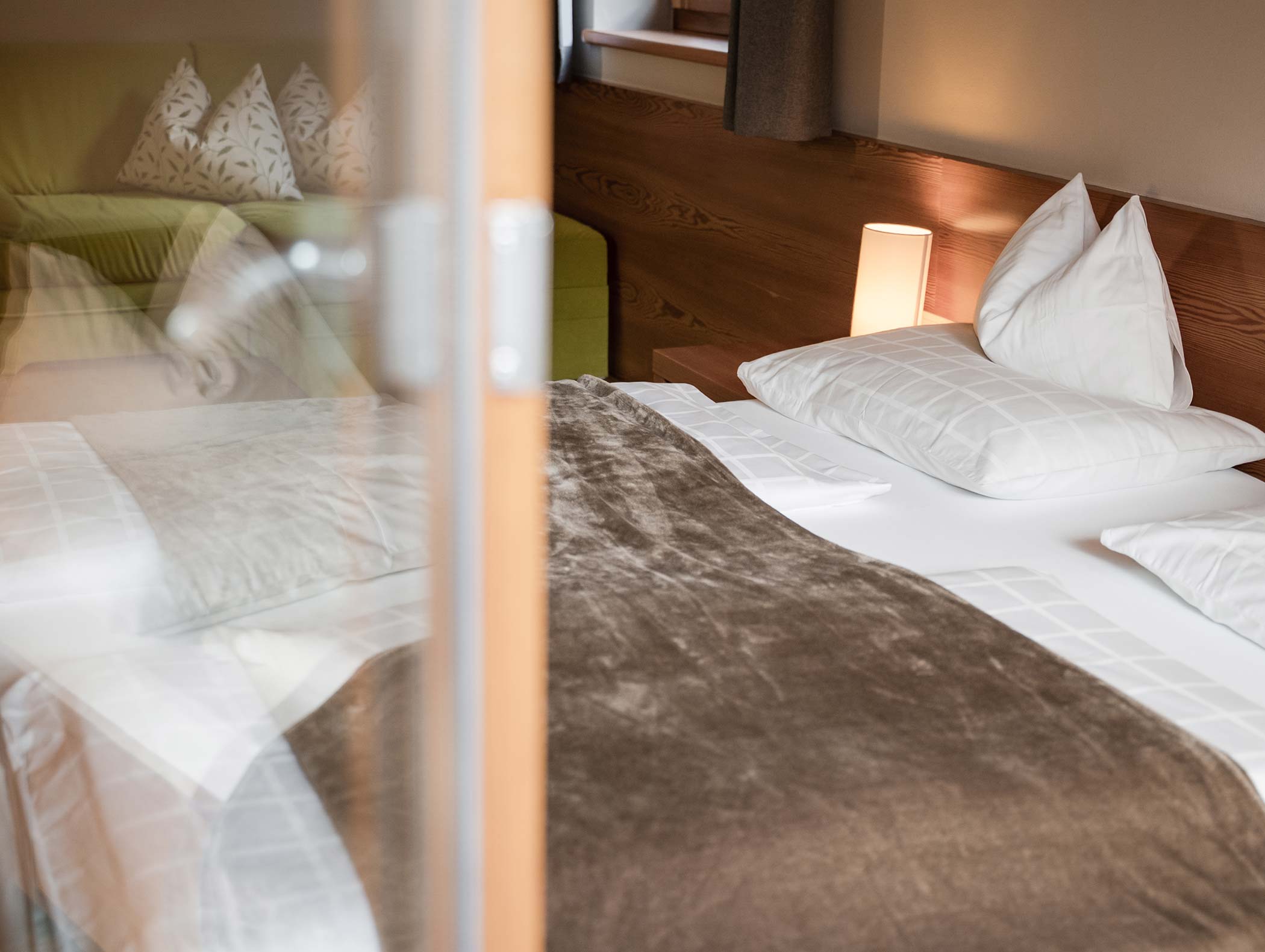 Accogliente letto ben fatto con cuscini bianchi, coperta marrone e lampada da comodino in una stanza dalle luci soffuse. - Hotel Moosmair