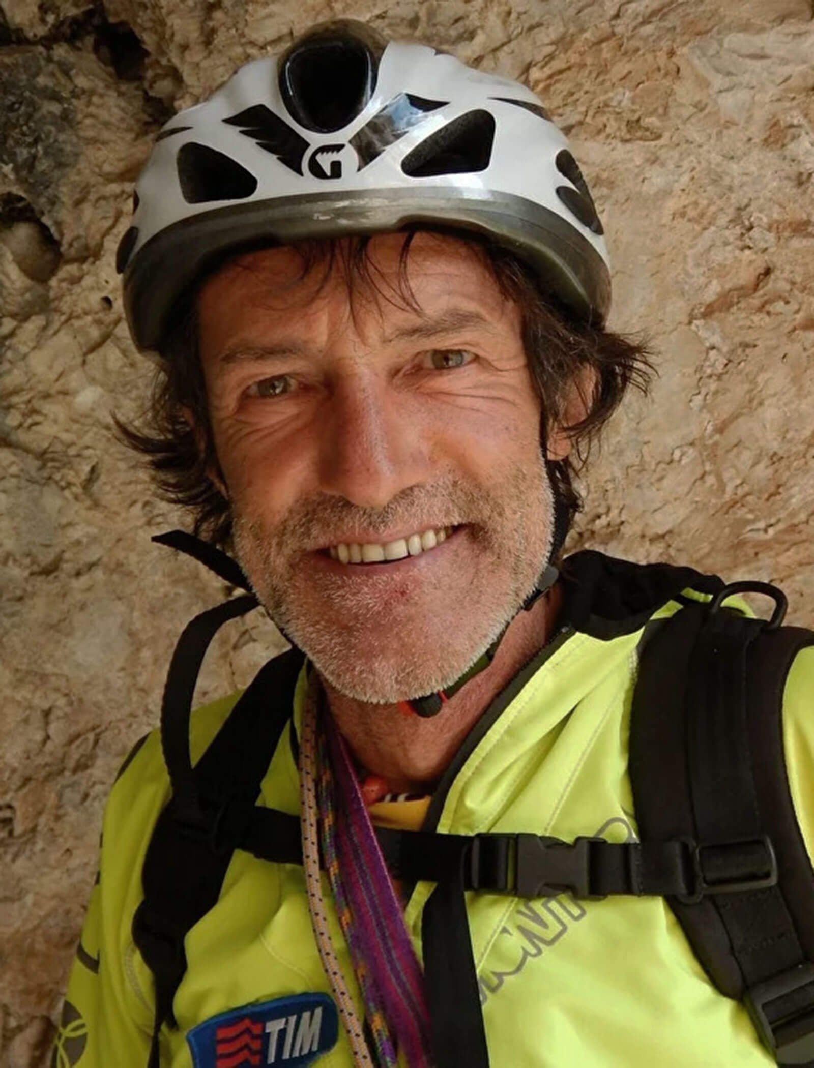Uomo sorridente con casco da bici e giacca gialla si trova davanti a uno sfondo roccioso. - Hotel Moosmair