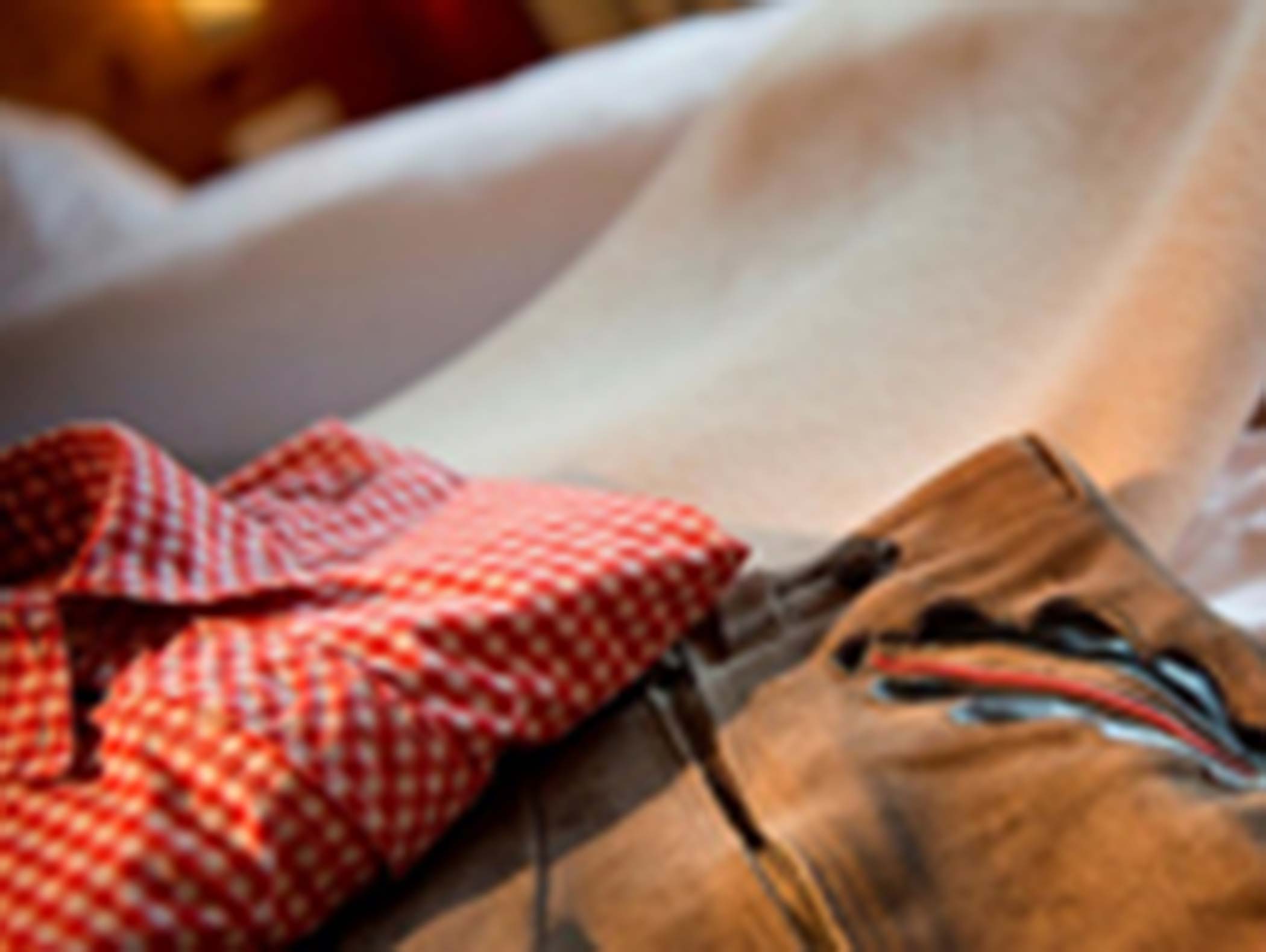 Camicia a scacchi rossa e pantaloni marroni con ricami stesi su un letto, immagine sfocata. - Hotel Moosmair