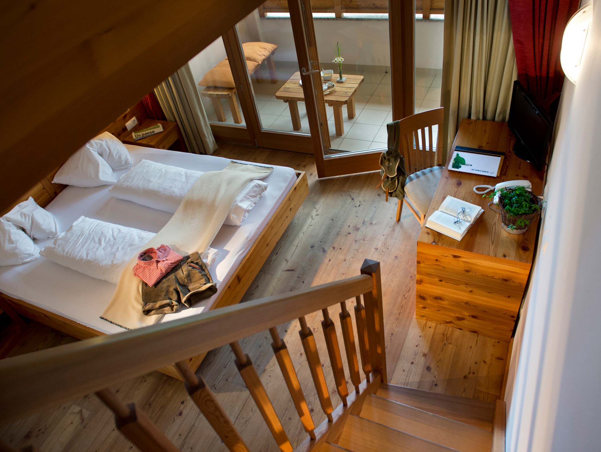 Accogliente camera in legno con letto matrimoniale, scrivania, sedia e vista sul balcone, visto da una scala sovrastante. - Hotel Moosmair