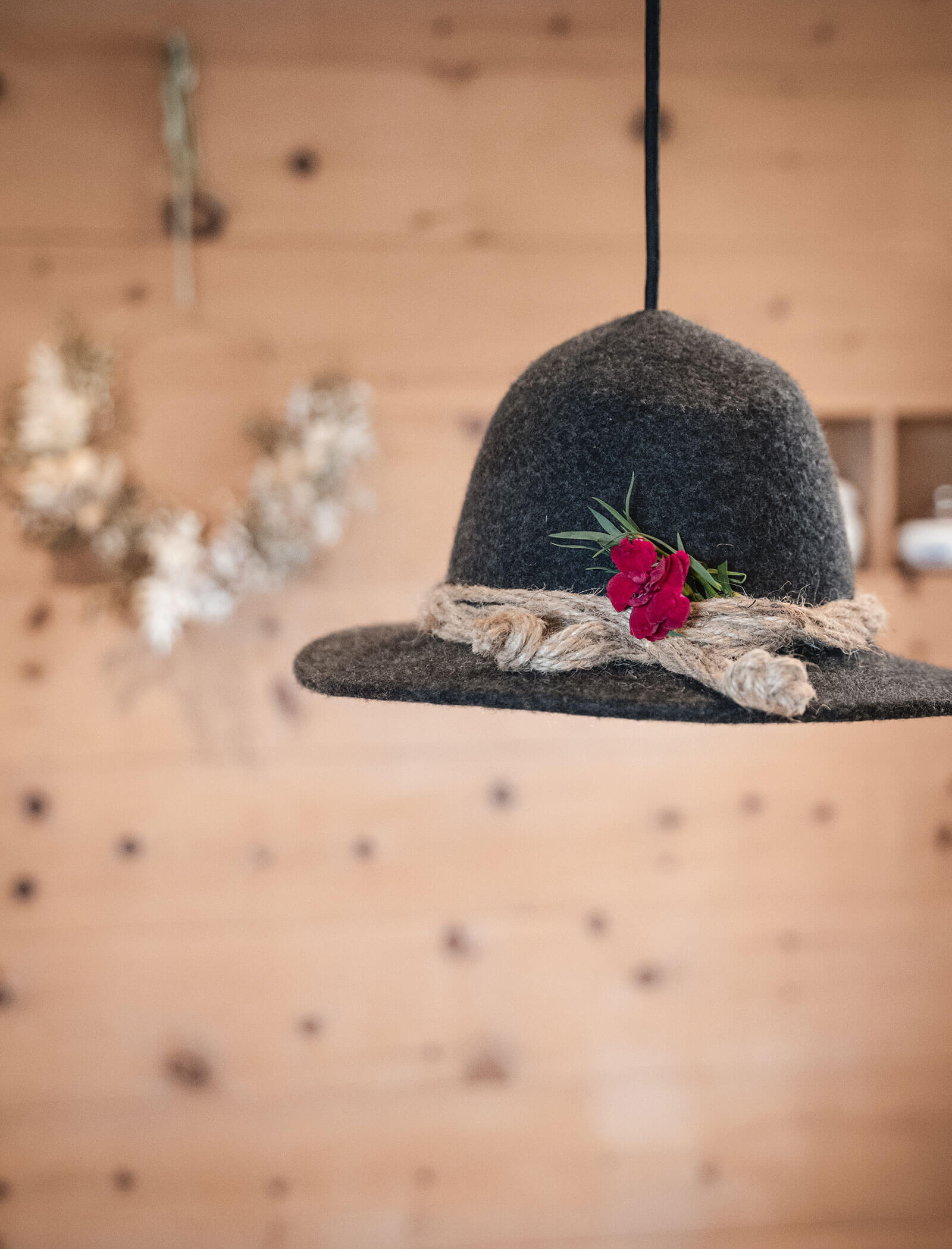 Cappello di feltro grigio con corda e fiore rosso appeso in casa su sfondo di una parete di legno. - Hotel Moosmair