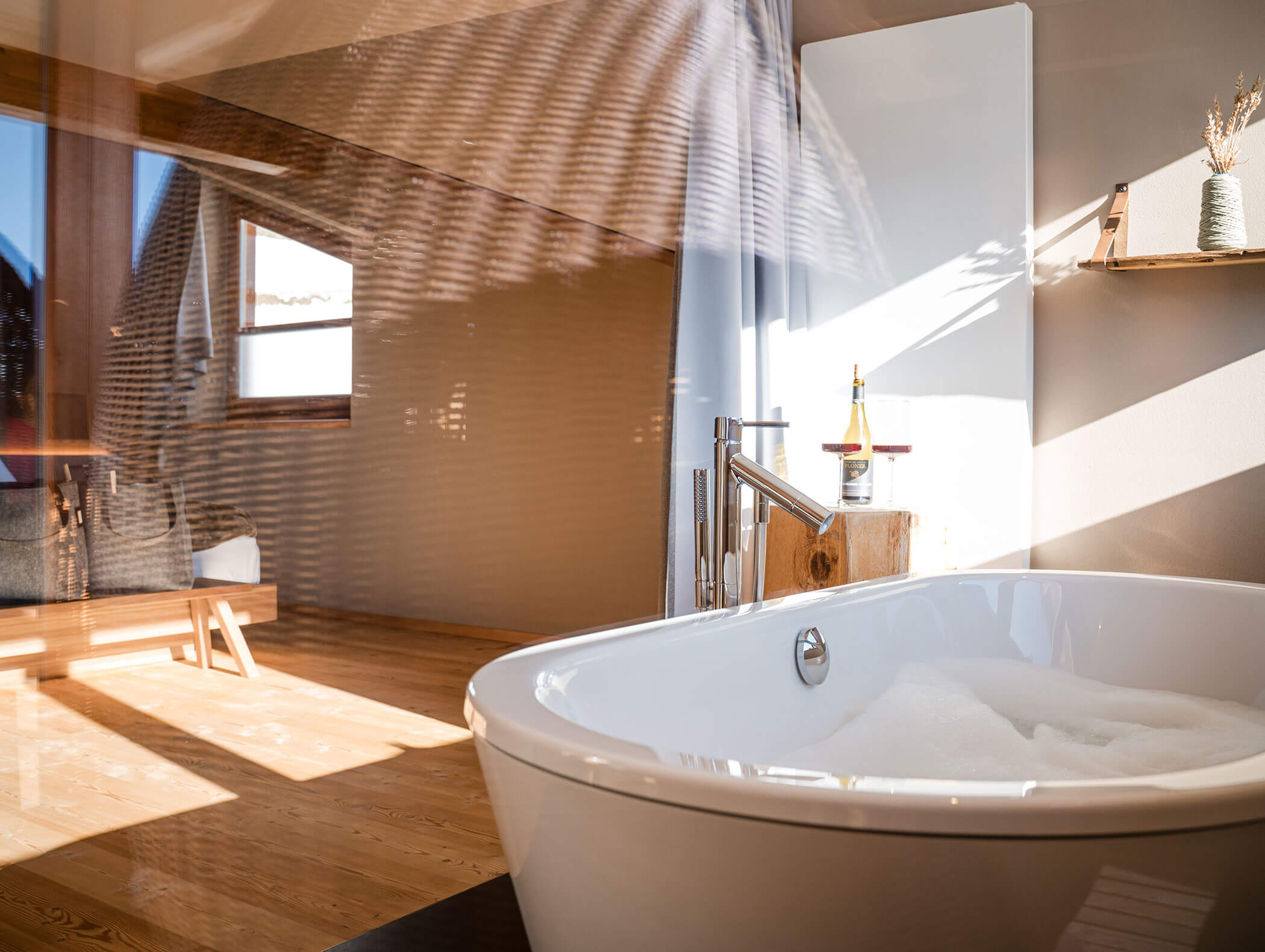 Un bagno illuminato dal sole con una vasca bianca piena di bolle e accenti in legno in uno spazio moderno e accogliente. - Hotel Moosmair