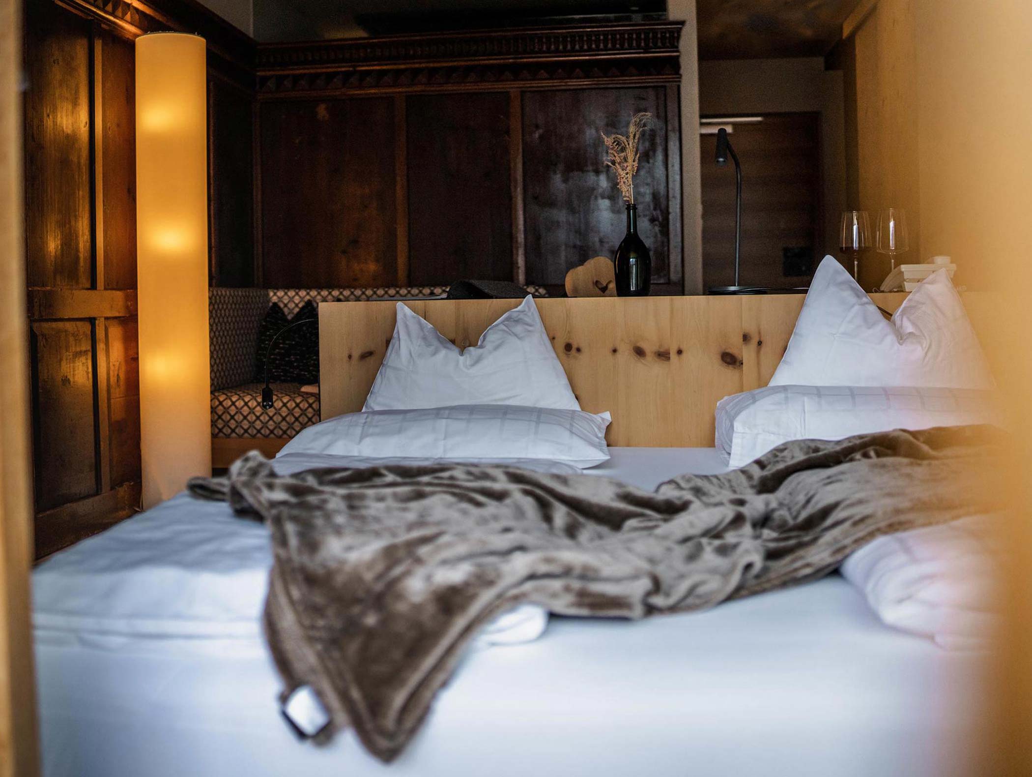 Un letto accogliente con cuscini bianchi e una coperta marrone in una stanza di legno rustica e caldamente illuminata. - Hotel Moosmair