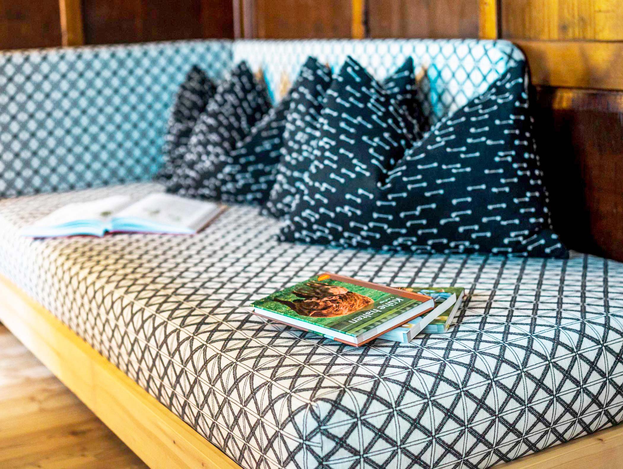 Un divano a fantasia con cuscini in bianco e nero e libri appoggiati sulla seduta in una stanza ben illuminata. - Hotel Moosmair