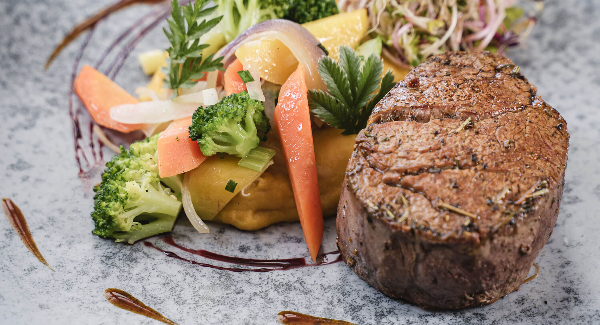 Gegrilltes Steak mit verschiedenen Gemüsesorten, Kartoffelpüree und Soße, kunstvoll auf einem grauen Teller angerichtet. - Hotel Moosmair