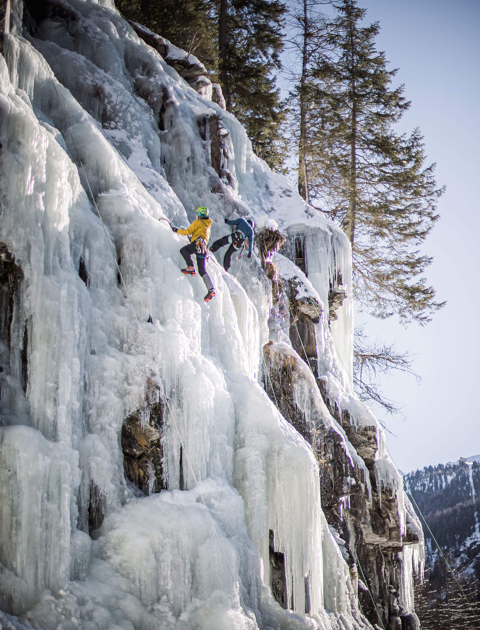 Due persone scalano una ripida e gelida cascata ghiacciata in un paesaggio montano innevato e circondato da alberi. - Hotel Moosmair