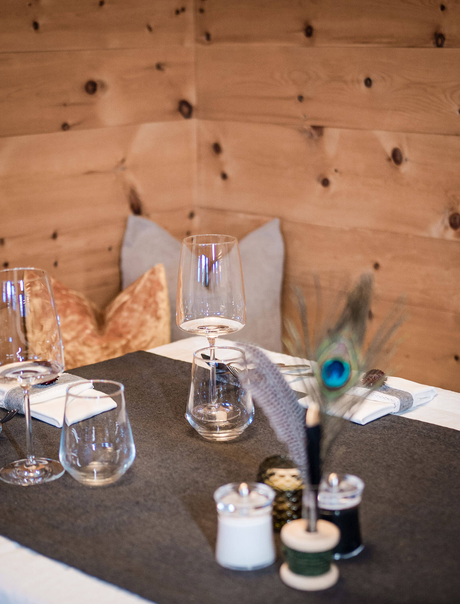 Elegant table setting with wine glasses, napkins, salt and pepper, and peacock feathers on a black table runner. - Hotel Moosmair