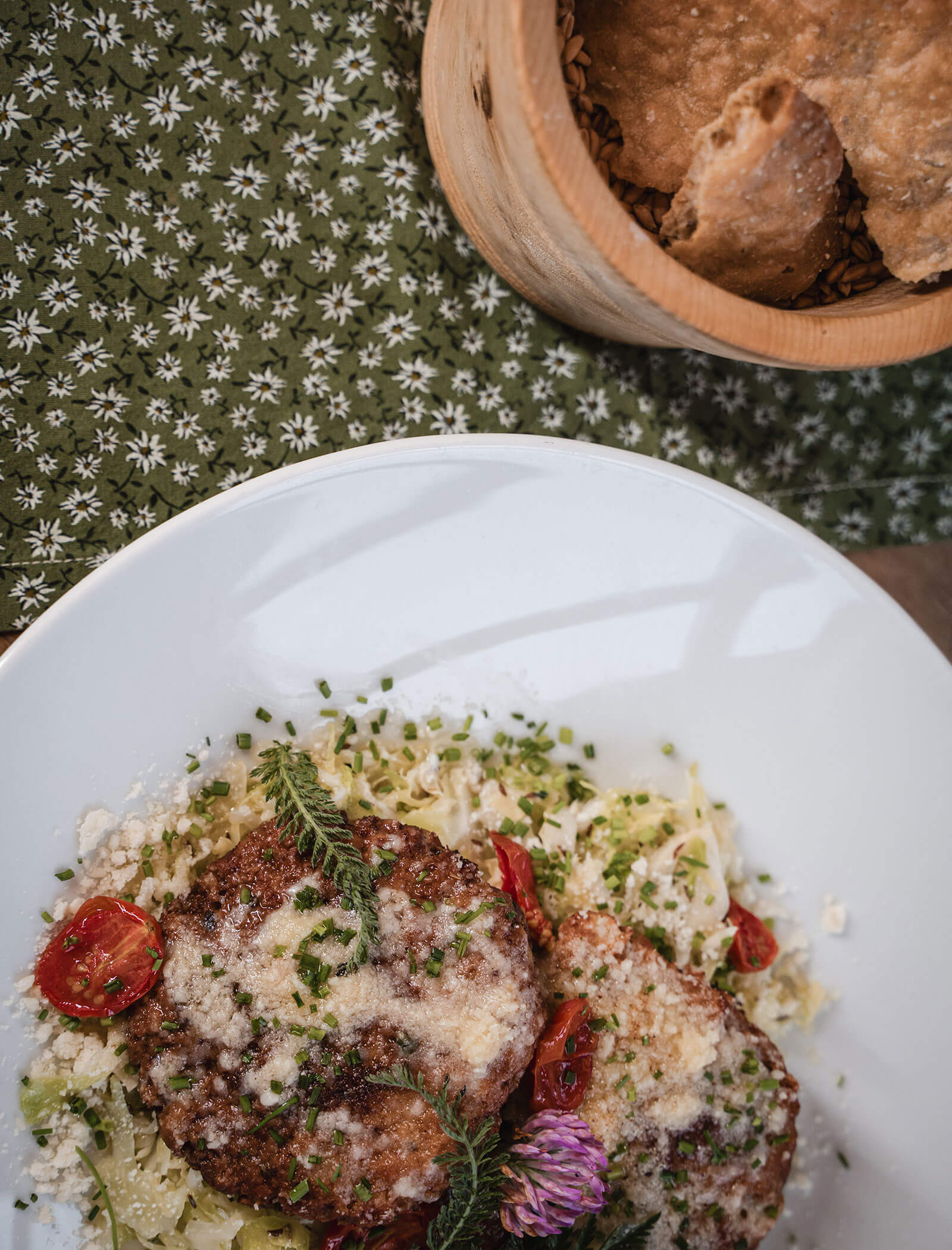 Two crispy patties with grated cheese, tomatoes, and herbs on cabbage, served with a basket of bread. - Hotel Moosmair
