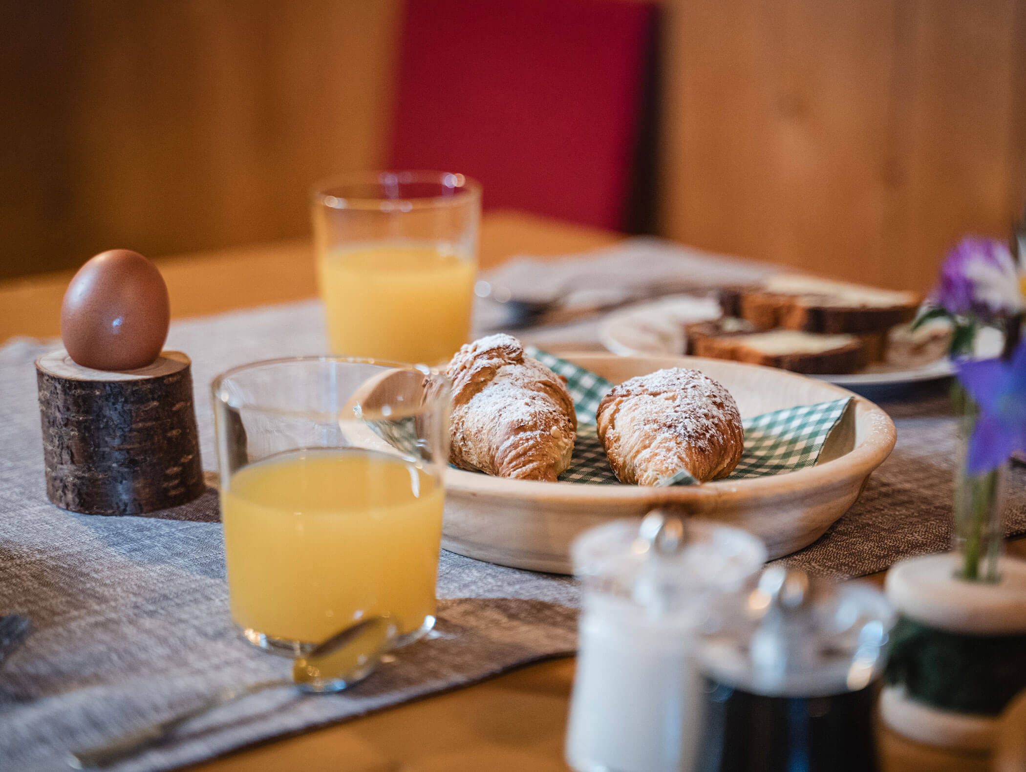 A breakfast table with juice, boiled egg, croissants with powdered sugar, and sliced bread. - Hotel Moosmair