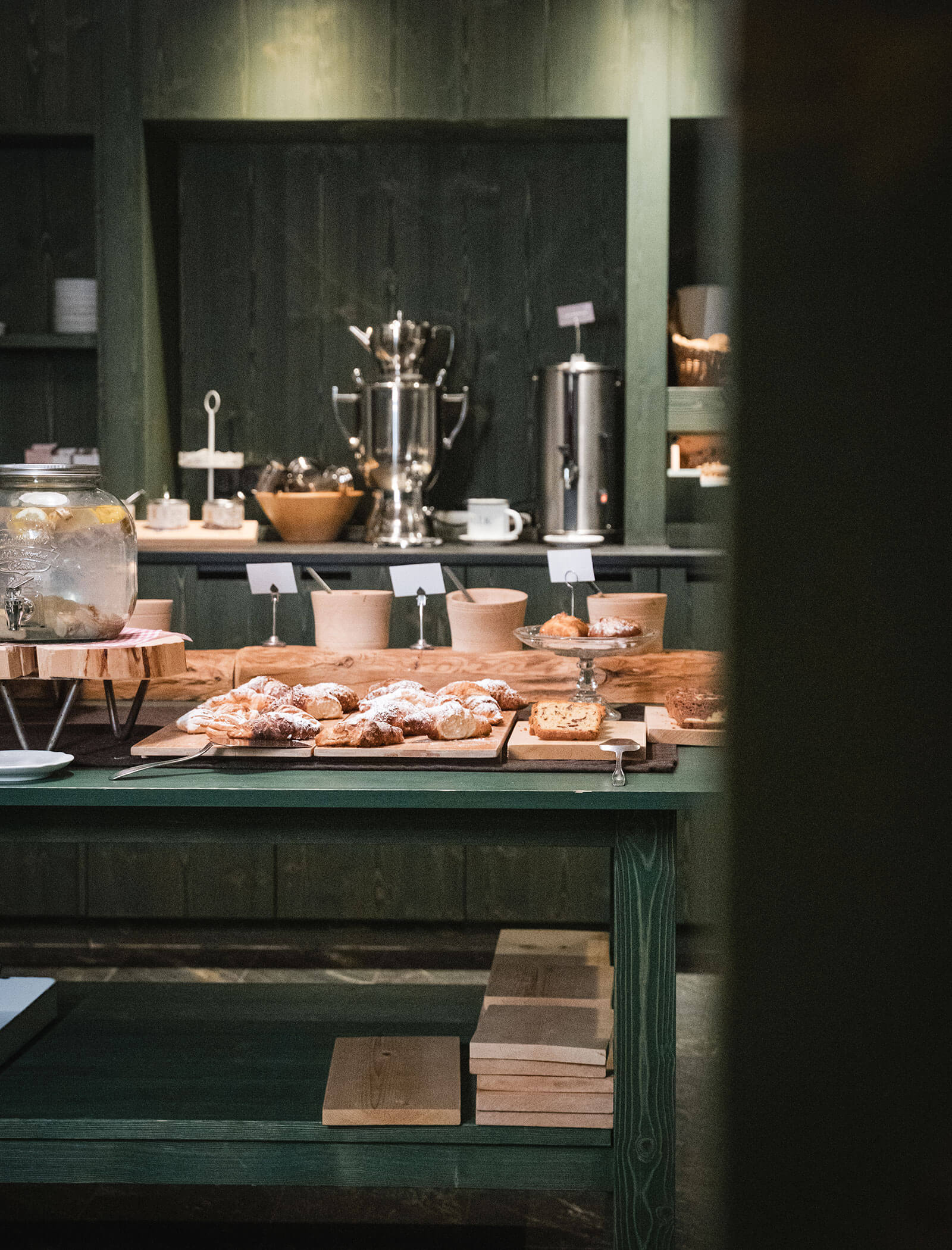 A wooden table with assorted pastries, bread, and coffee dispensers set up for a breakfast buffet. - Hotel Moosmair