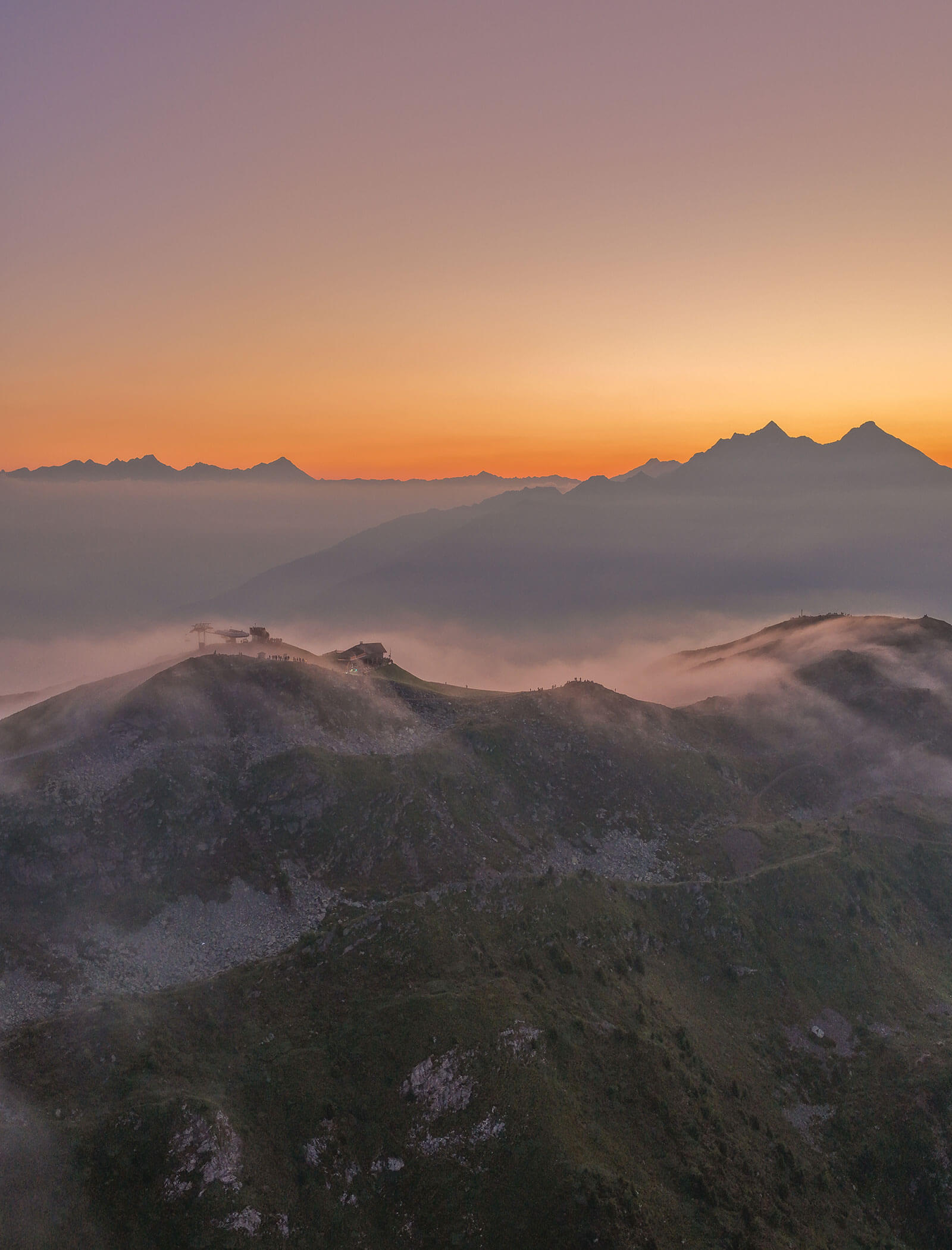 Mountain peaks at sunrise with mist covering the hills and an orange sky in the background. - Hotel Moosmair