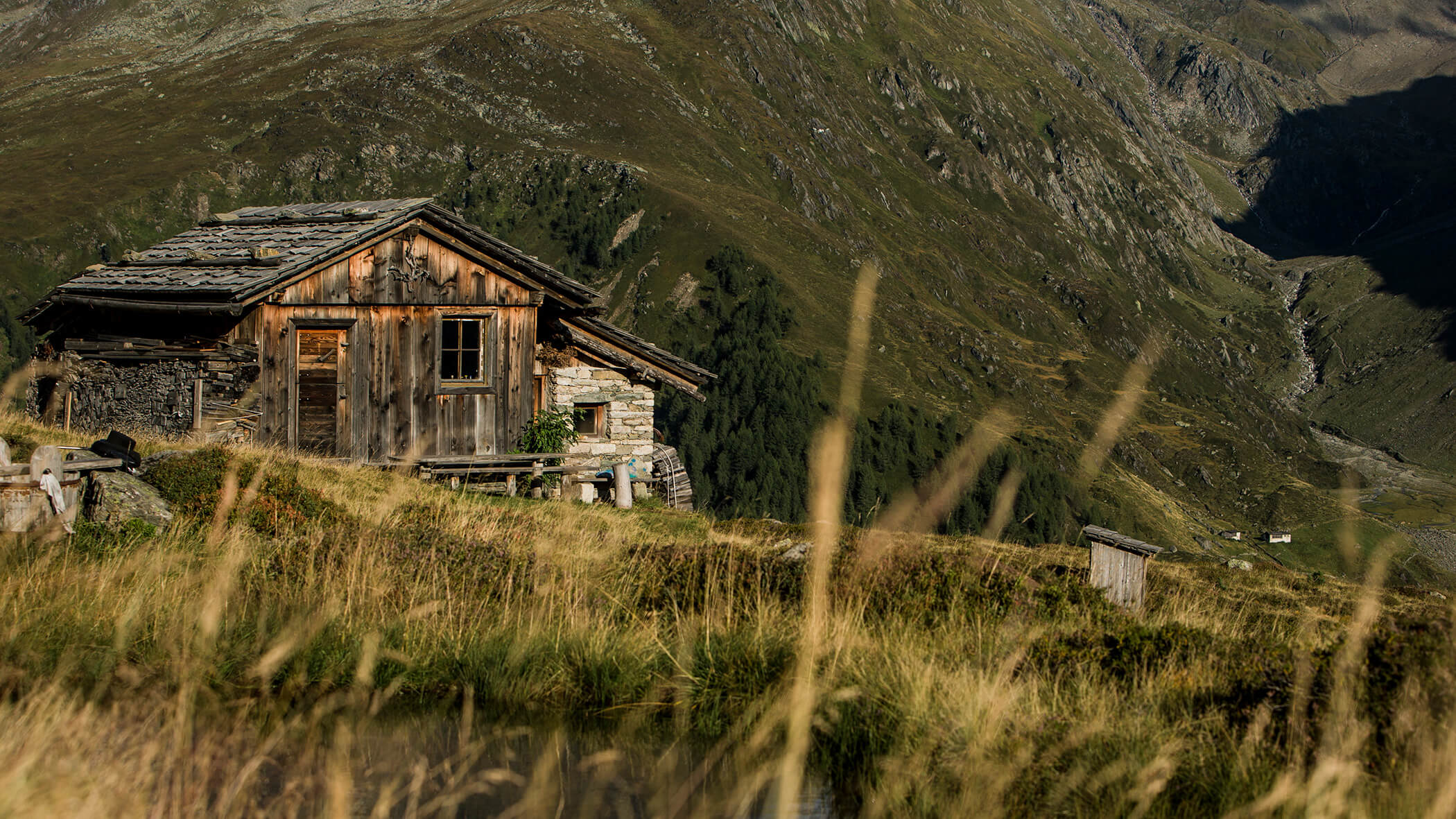 Eine rustikale Holzhütte steht auf einem grasbewachsenen Hügel mit Bergen im Hintergrund. - Hotel Moosmair