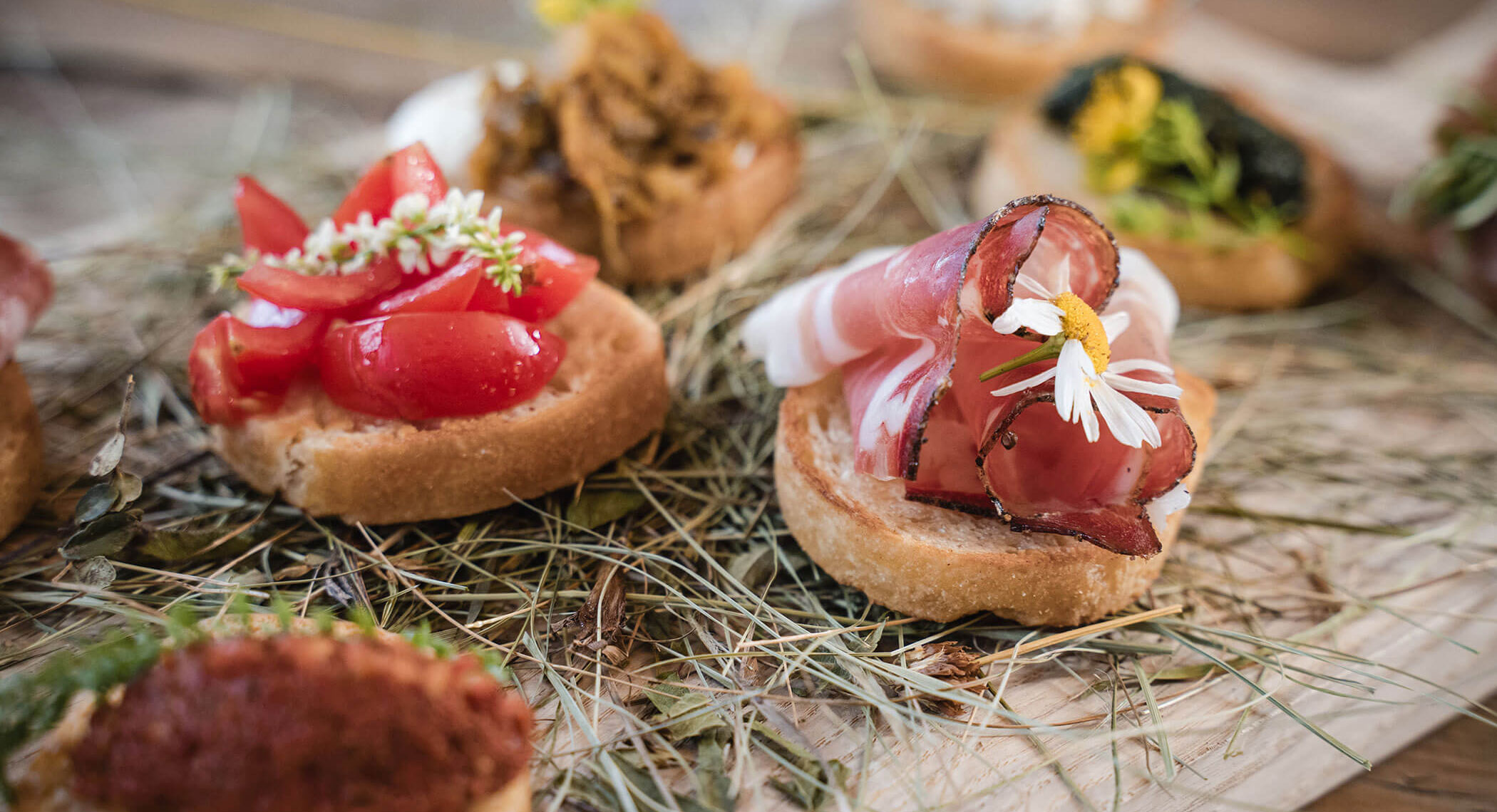 Antipasti gourmet assortiti su pane, conditi con salumi, pomodori, erbe e fiori commestibili su una superficie rustica. - Hotel Moosmair
