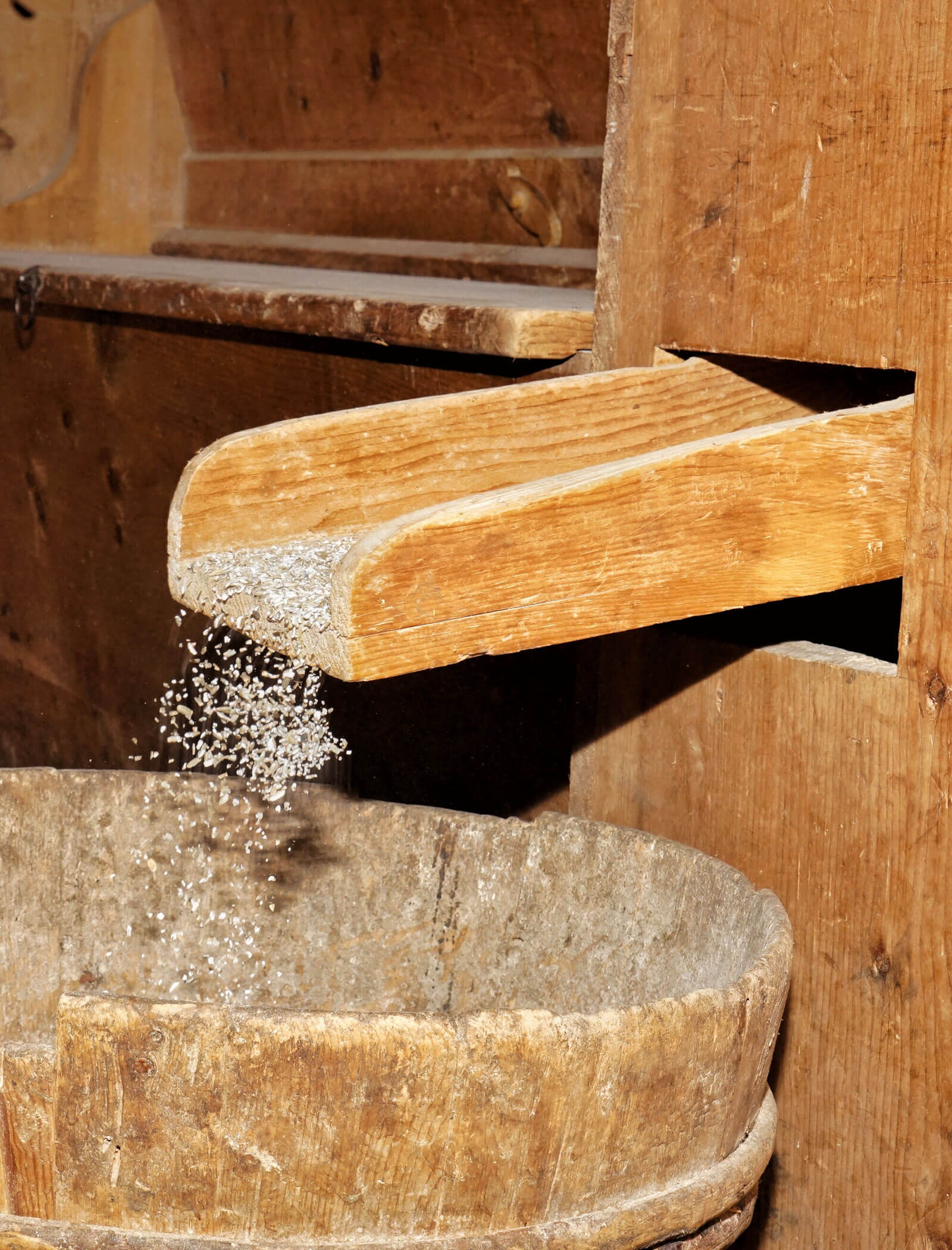 Il grano viene versato da uno scivolo di legno in un barile o contenitore di legno rustico. - Hotel Moosmair