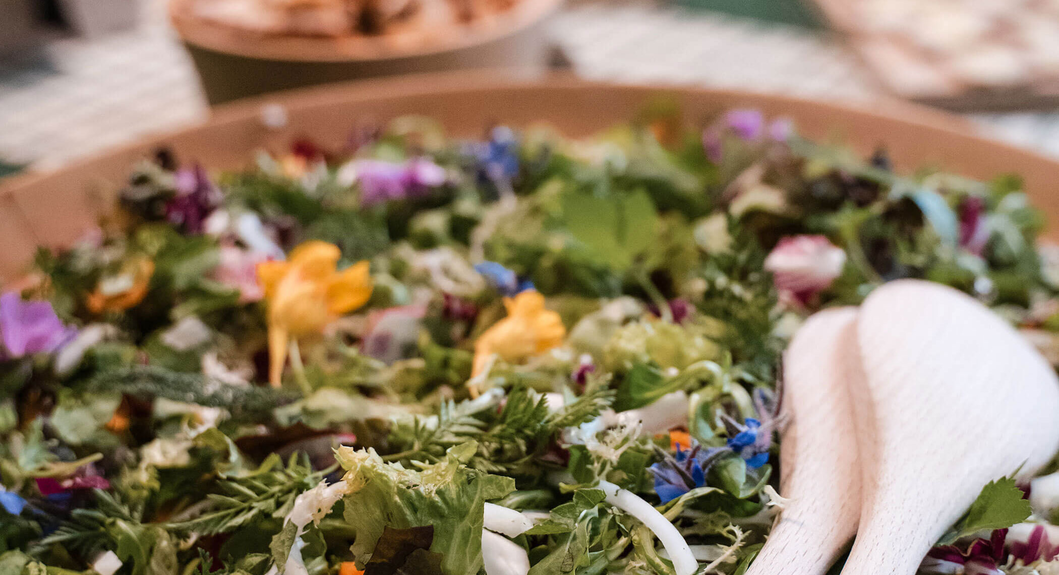 Un'insalata fresca con verdure miste, fiori commestibili e utensili di legno in una ciotola. - Hotel Moosmair