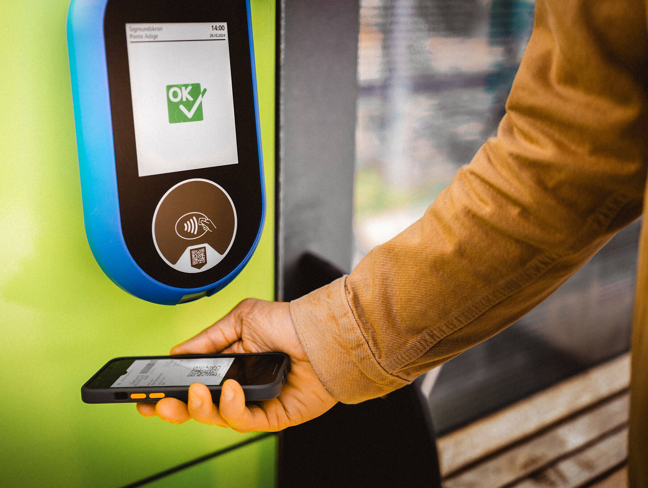 Eine Person hält ein Smartphone mit einem QR-Code in der Nähe eines Terminals für kontaktloses Bezahlen mit einem OK-Zeichen. - Hotel Moosmair
