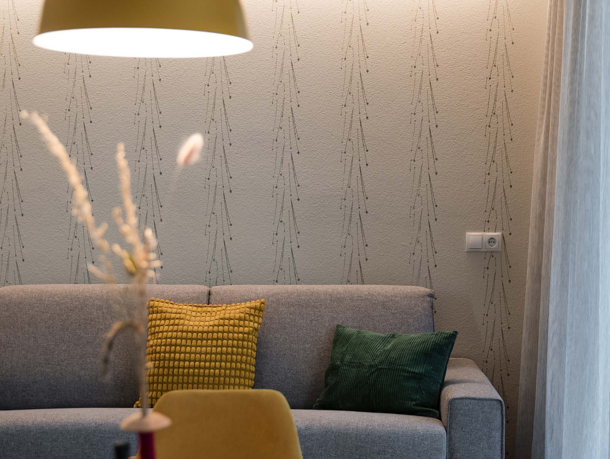 Un divano grigio con cuscini gialli e verdi è appoggiato su una parete a motivi sotto una luce soffusa. - Hotel Moosmair