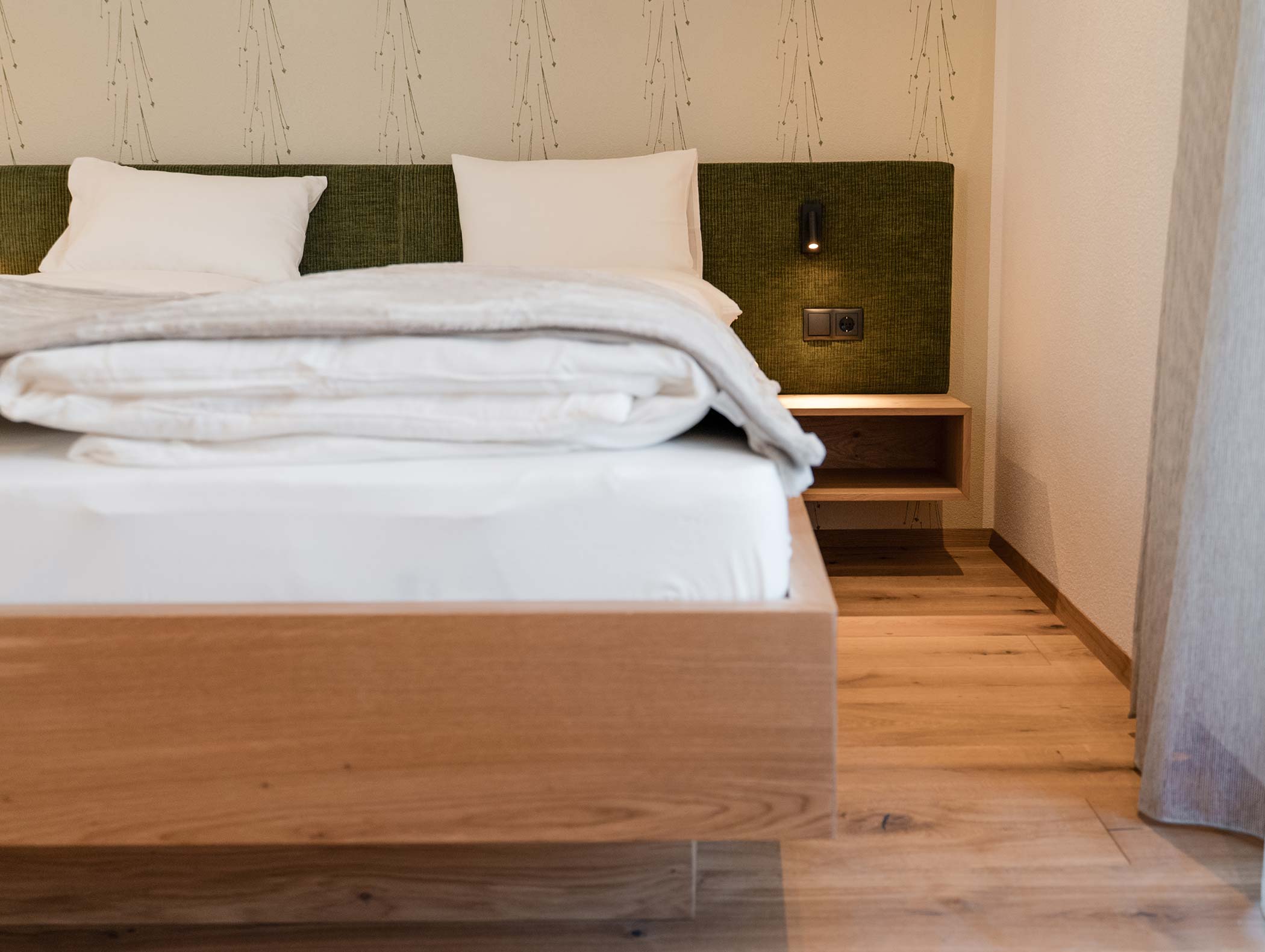 Camera da letto minimalista con letto in legno, testata verde, biancheria da letto bianca e comodino galleggiante. - Hotel Moosmair