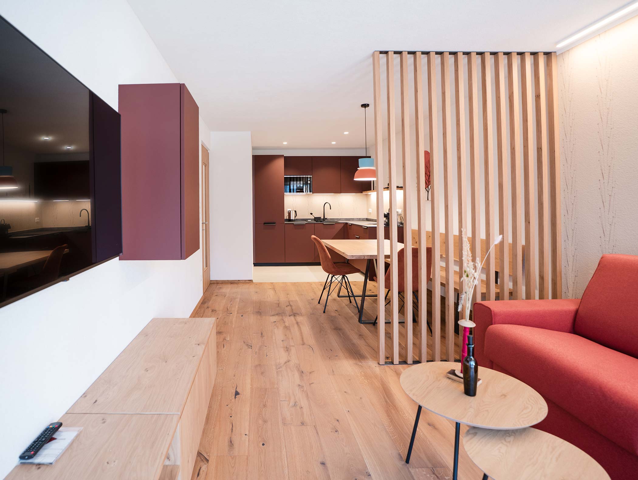 Moderno soggiorno e cucina a pianta aperta con pavimento in legno, divano arancione e divisorio in doghe di legno. - Hotel Moosmair