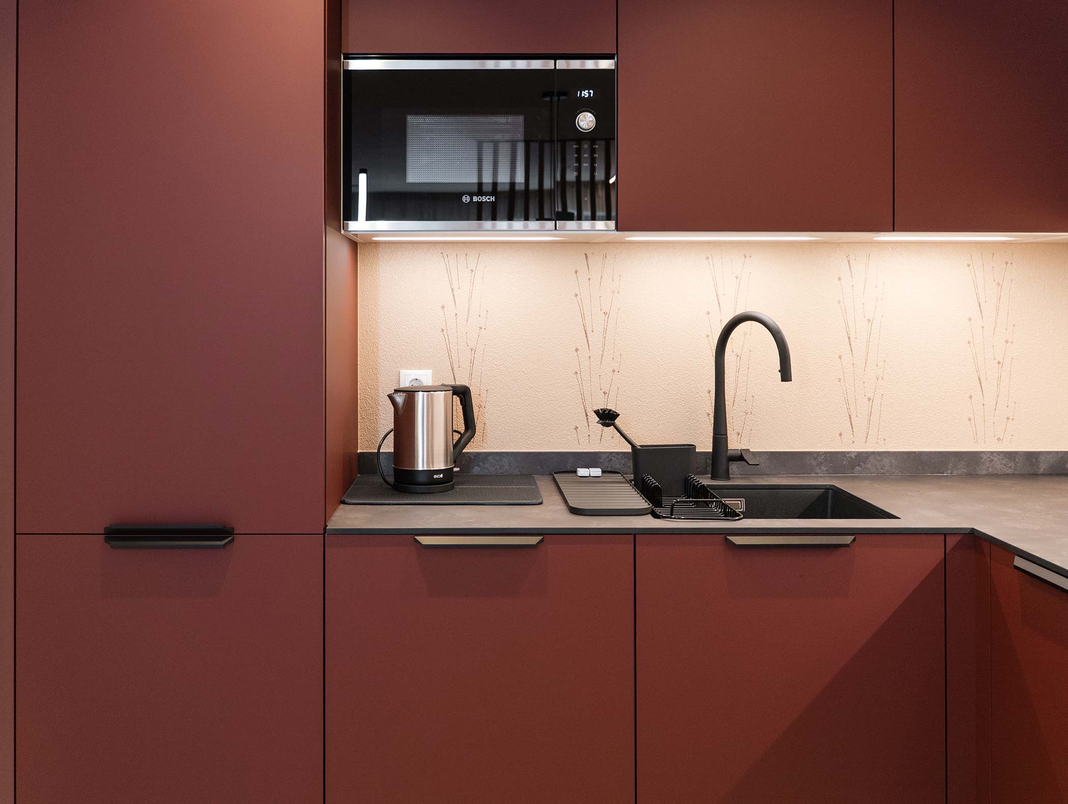 Cucina moderna con armadietti marroni, lavello nero, bollitore elettrico e microonde incorporato. - Hotel Moosmair