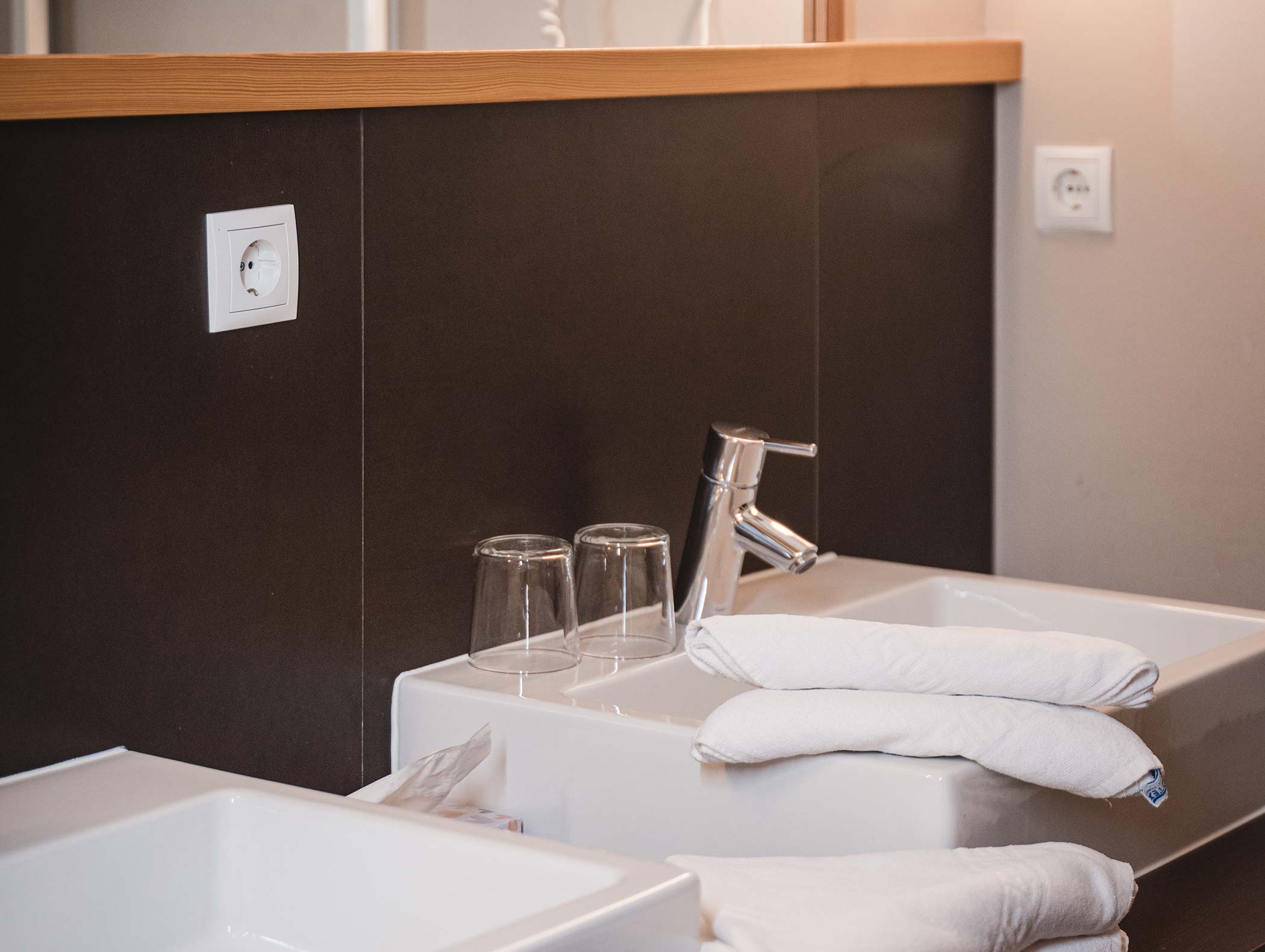 Due lavandini con asciugamani piegati, due bicchieri e un rubinetto moderno in un ambiente bagno pulito. - Hotel Moosmair