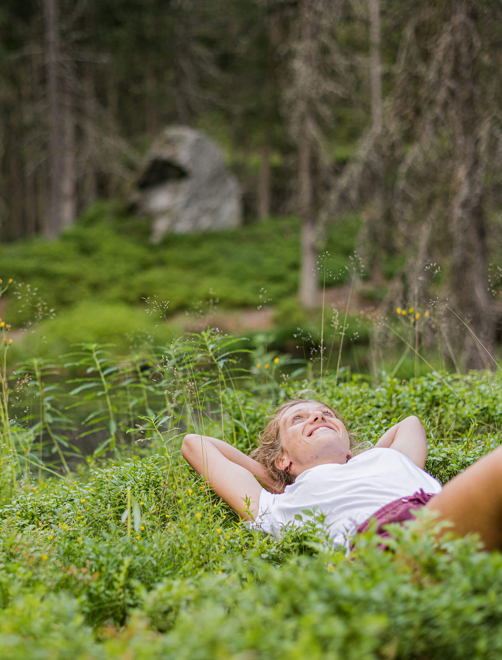 Woman lying on her back in green grass, smiling and relaxing in a lush forest clearing. - Hotel Moosmair
