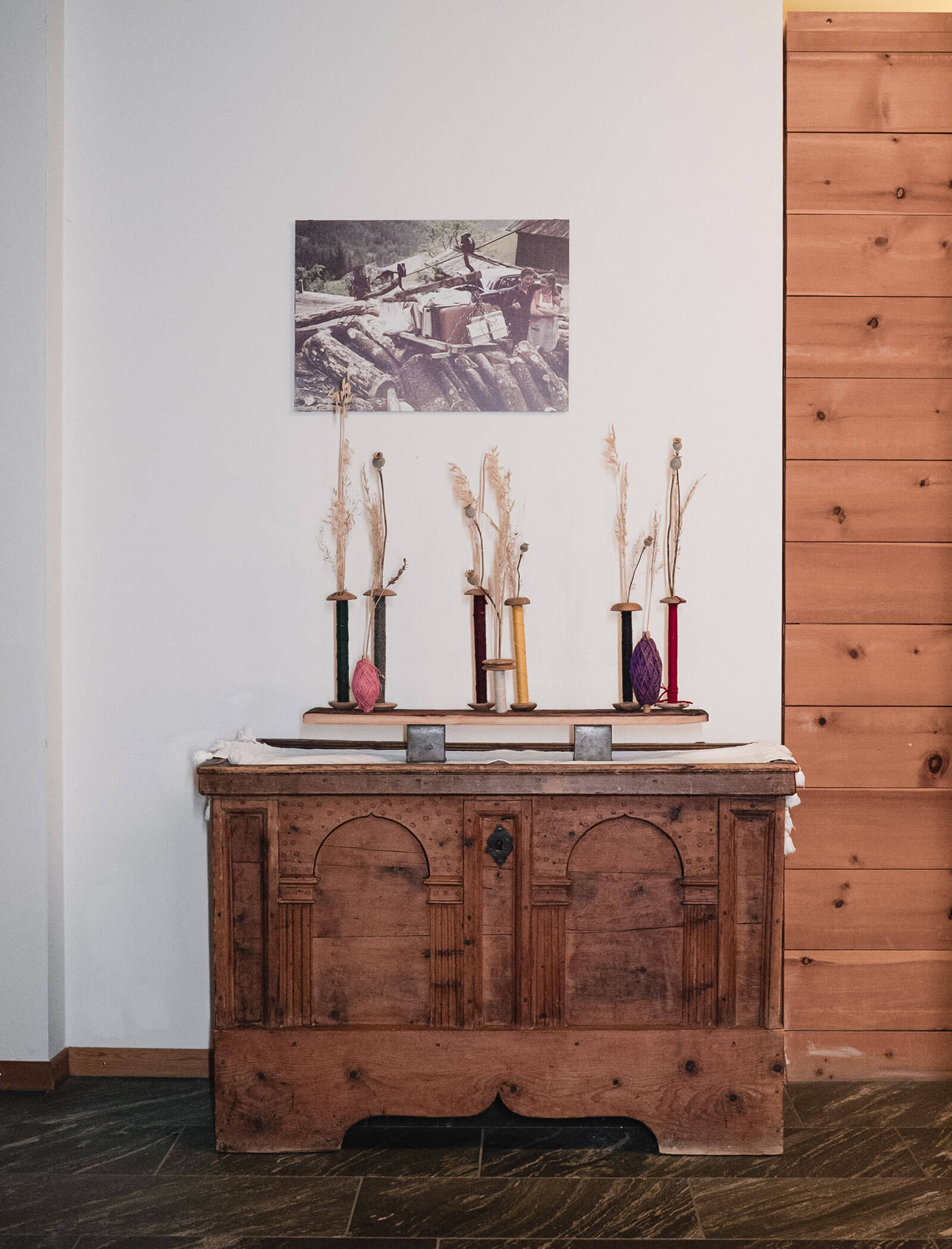A wooden chest with dried plants in vases, books, and a historical photo hanging above on a white wall. - Hotel Moosmair