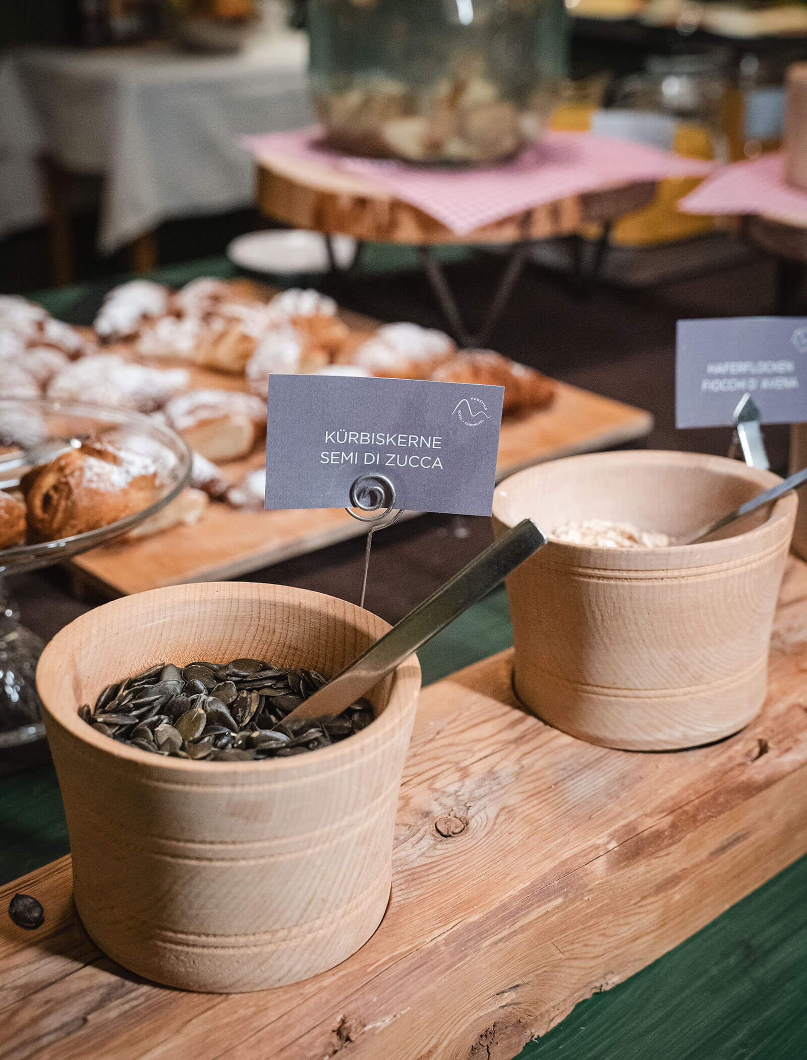 Wooden bowls with metal spoons hold pumpkin seeds and flour on a rustic table at a breakfast buffet. - Hotel Moosmair