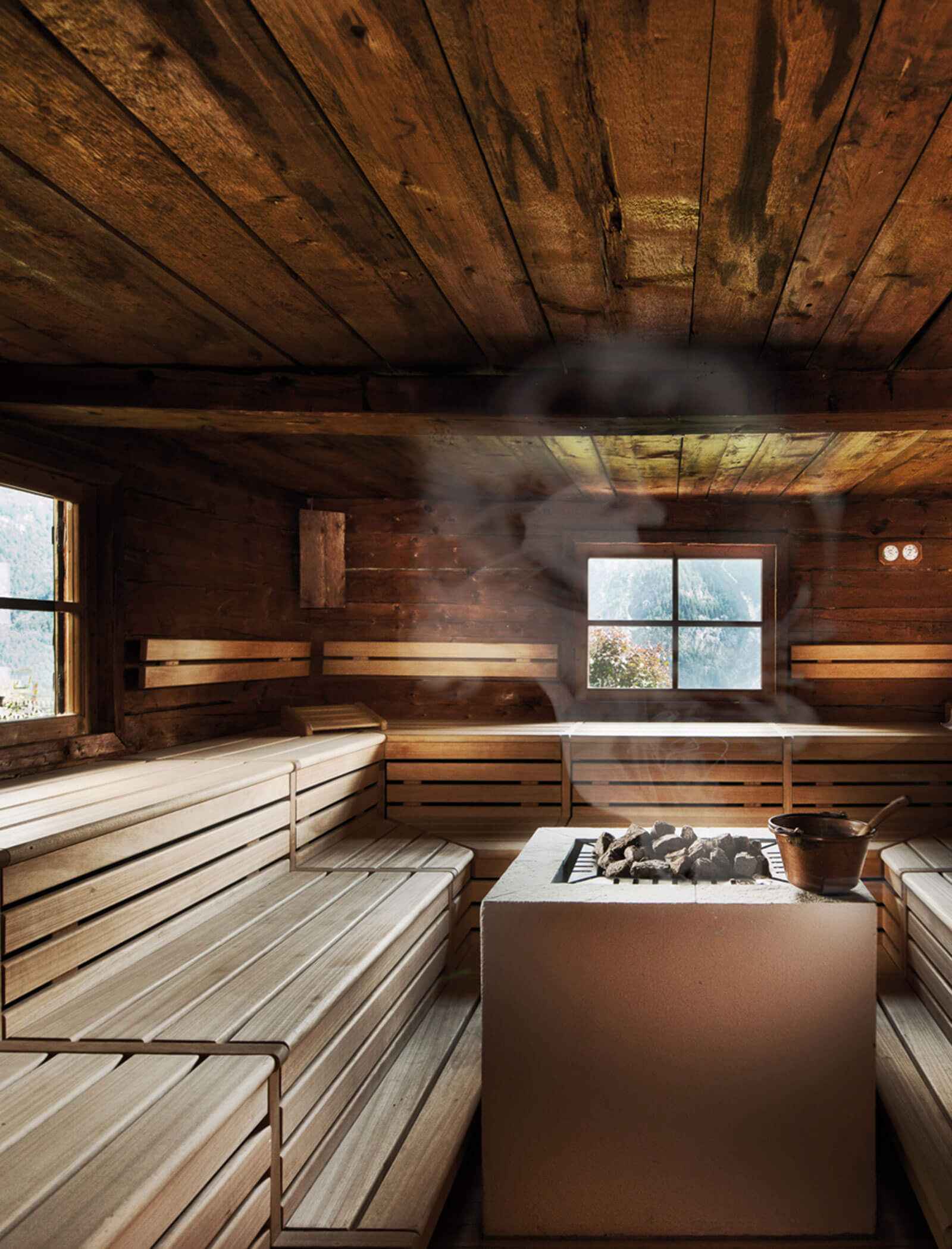 Das Innere einer Holzsauna mit Bänken, einem beheizten Steinofen und in der Mitte aufsteigendem Dampf. - Hotel Moosmair