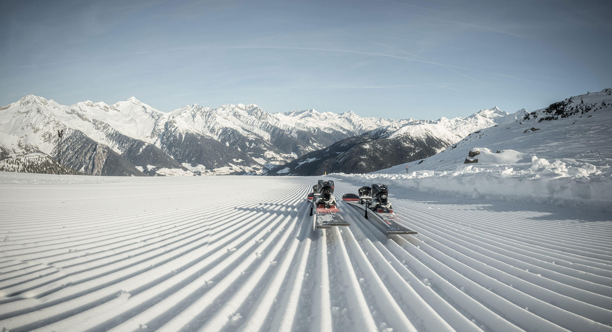 Due paia di sci appoggiati sulla neve appena battuta con le montagne e il cielo azzurro sullo sfondo. - Hotel Moosmair