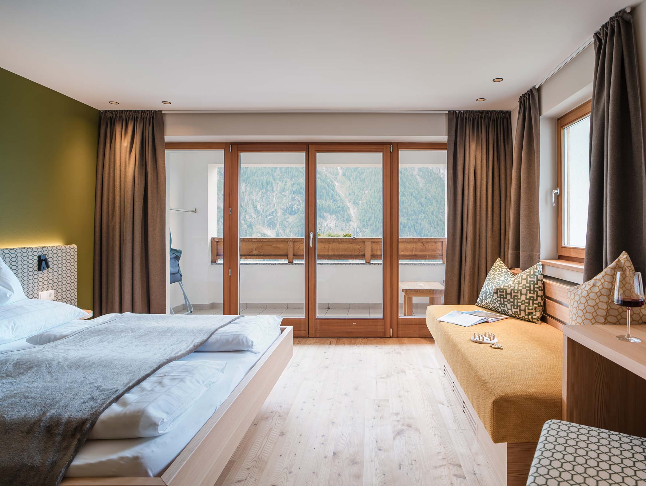 Moderna camera d'albergo con letto matrimoniale, pavimenti in legno, balcone e vista sulle montagne attraverso grandi porte di vetro. - Hotel Moosmair