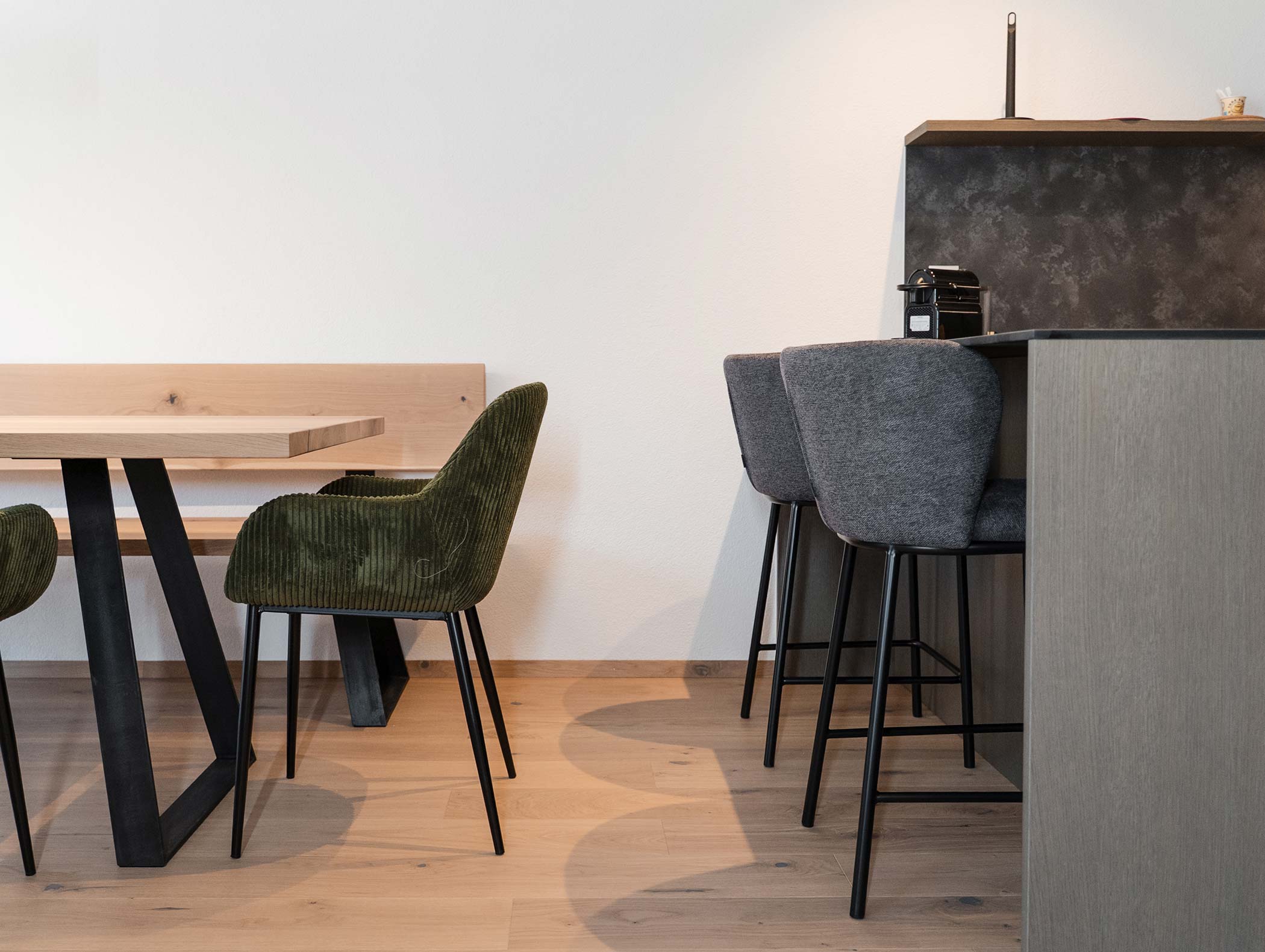 Zona pranzo moderna con tavolo in legno, sedia verde e sgabelli da bar grigi su un pavimento in legno chiaro. - Hotel Moosmair
