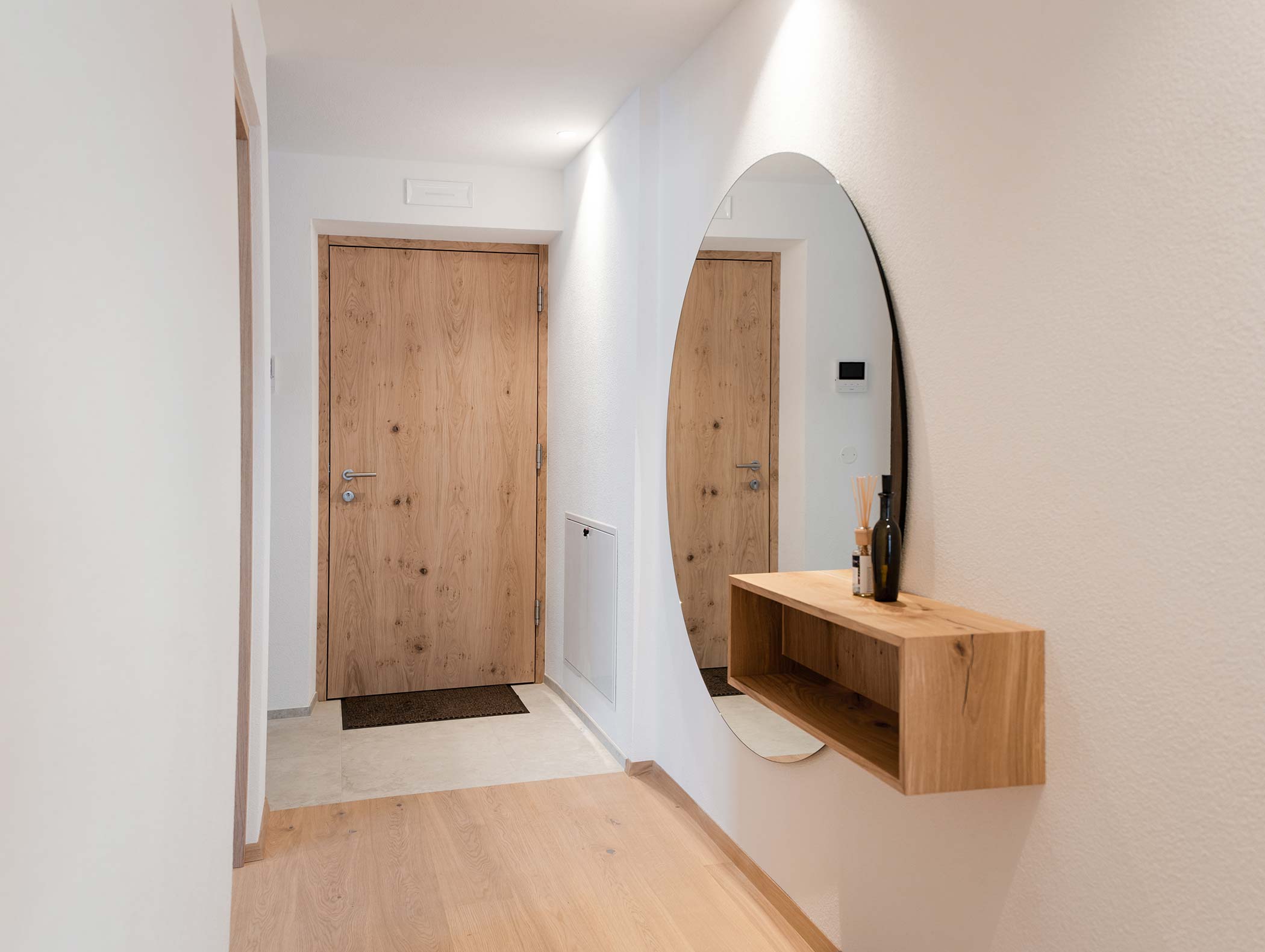 Corridoio minimalista con porte in legno, uno specchio rotondo a parete e una mensola galleggiante in legno con oggetti d'arredo. - Hotel Moosmair