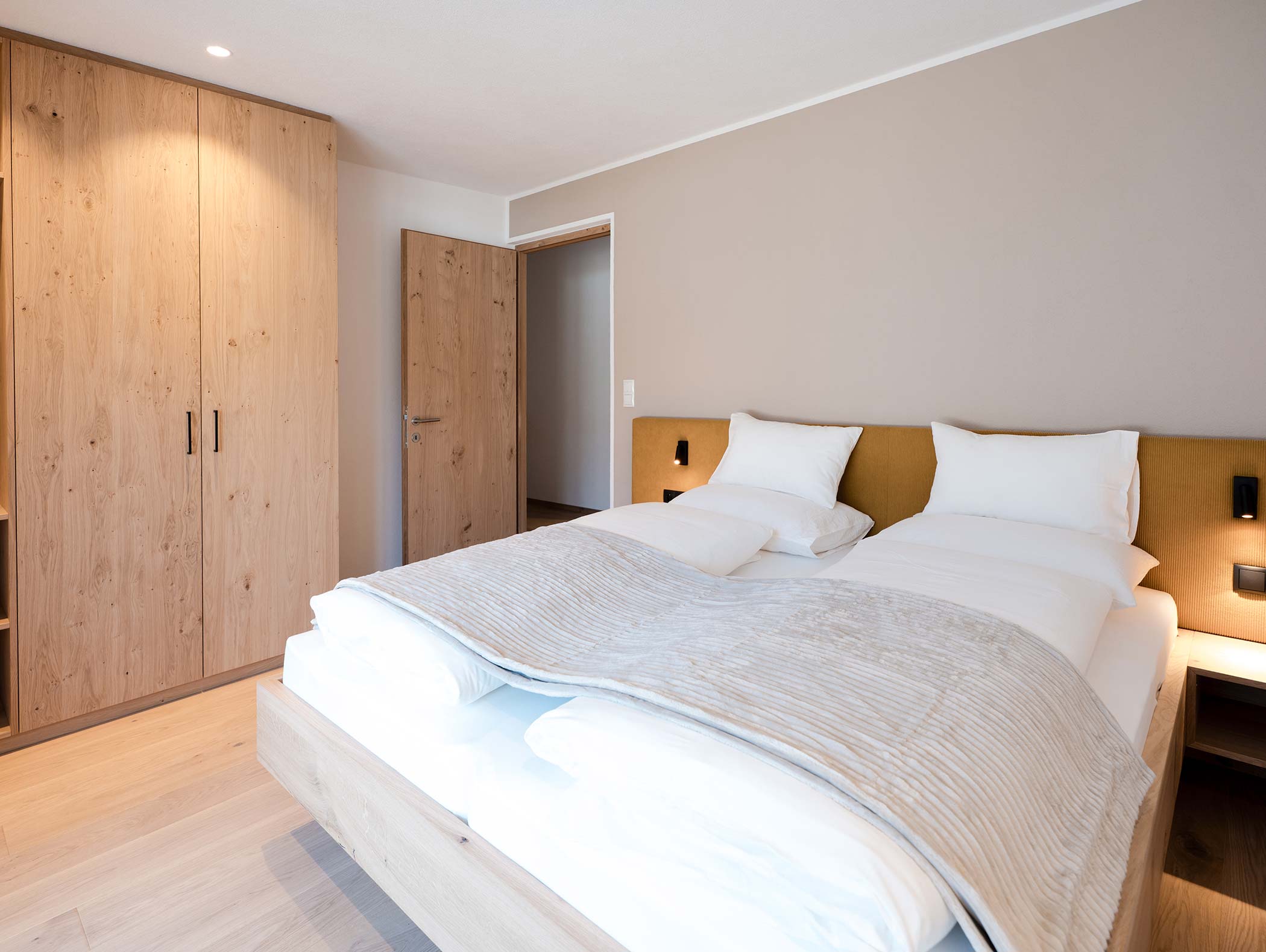 Camera minimalista con letto matrimoniale, armadio in legno, pareti beige e luce naturale soffusa. - Hotel Moosmair