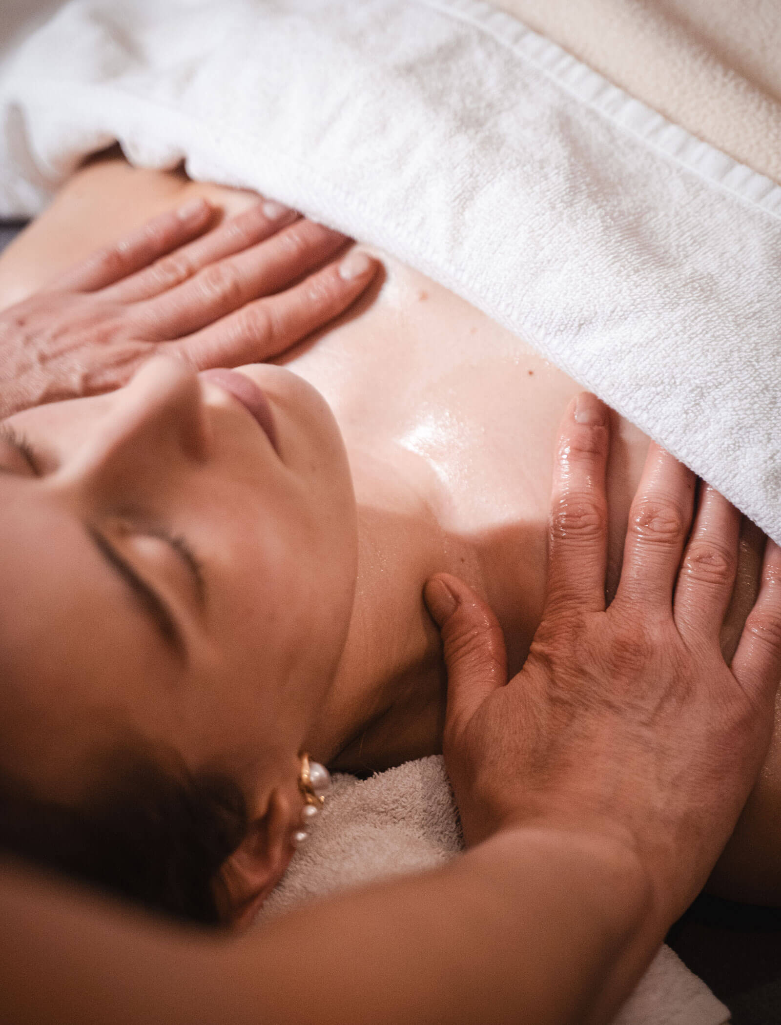 Eine Person erhält eine entspannende Brust- und Schultermassage im Liegen, zugedeckt mit einem weißen Handtuch. - Hotel Moosmair
