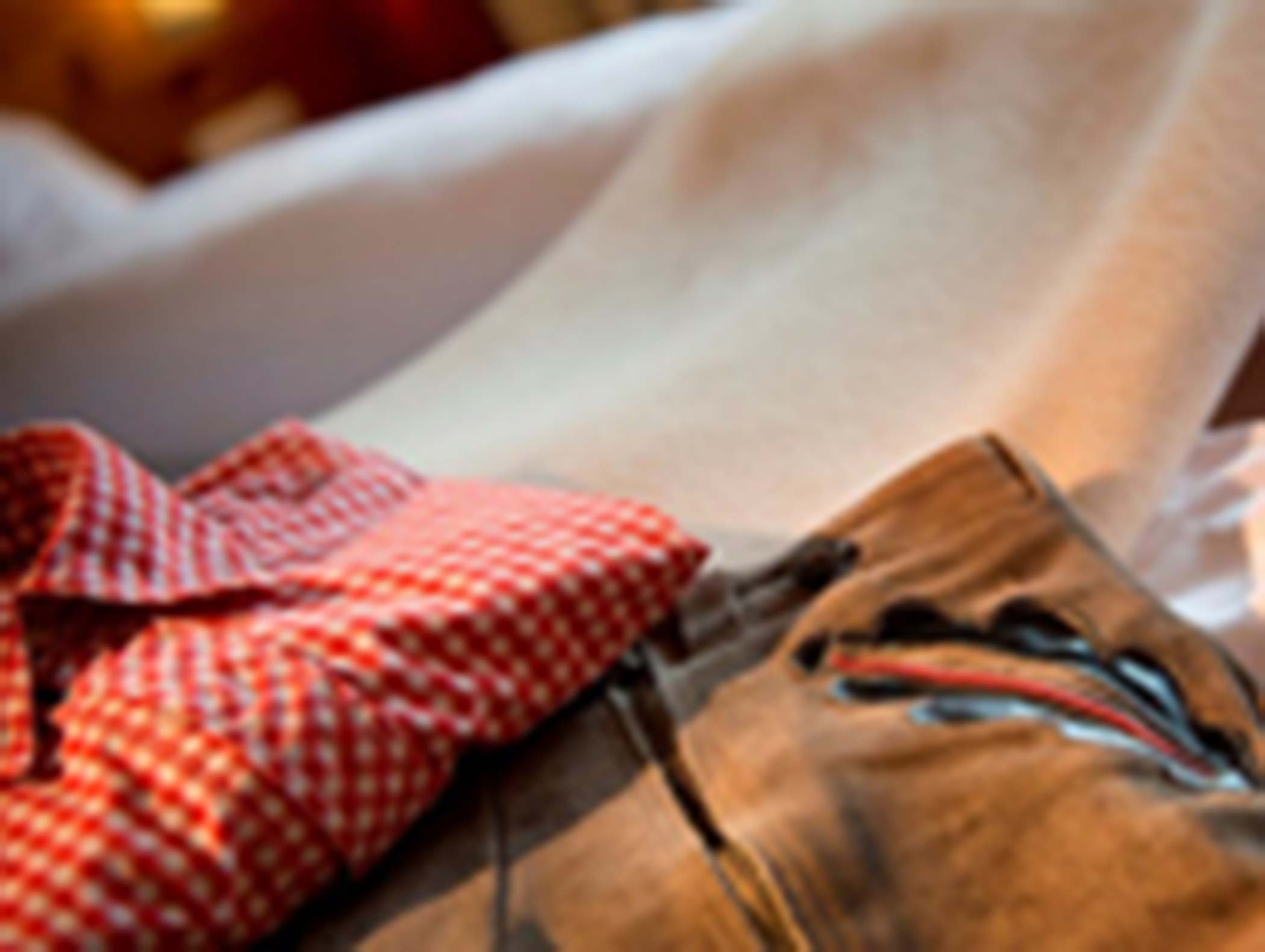 Camicia a scacchi rossa e pantaloni marroni con ricami adagiati su una superficie bianca, immagine sfocata. - Hotel Moosmair