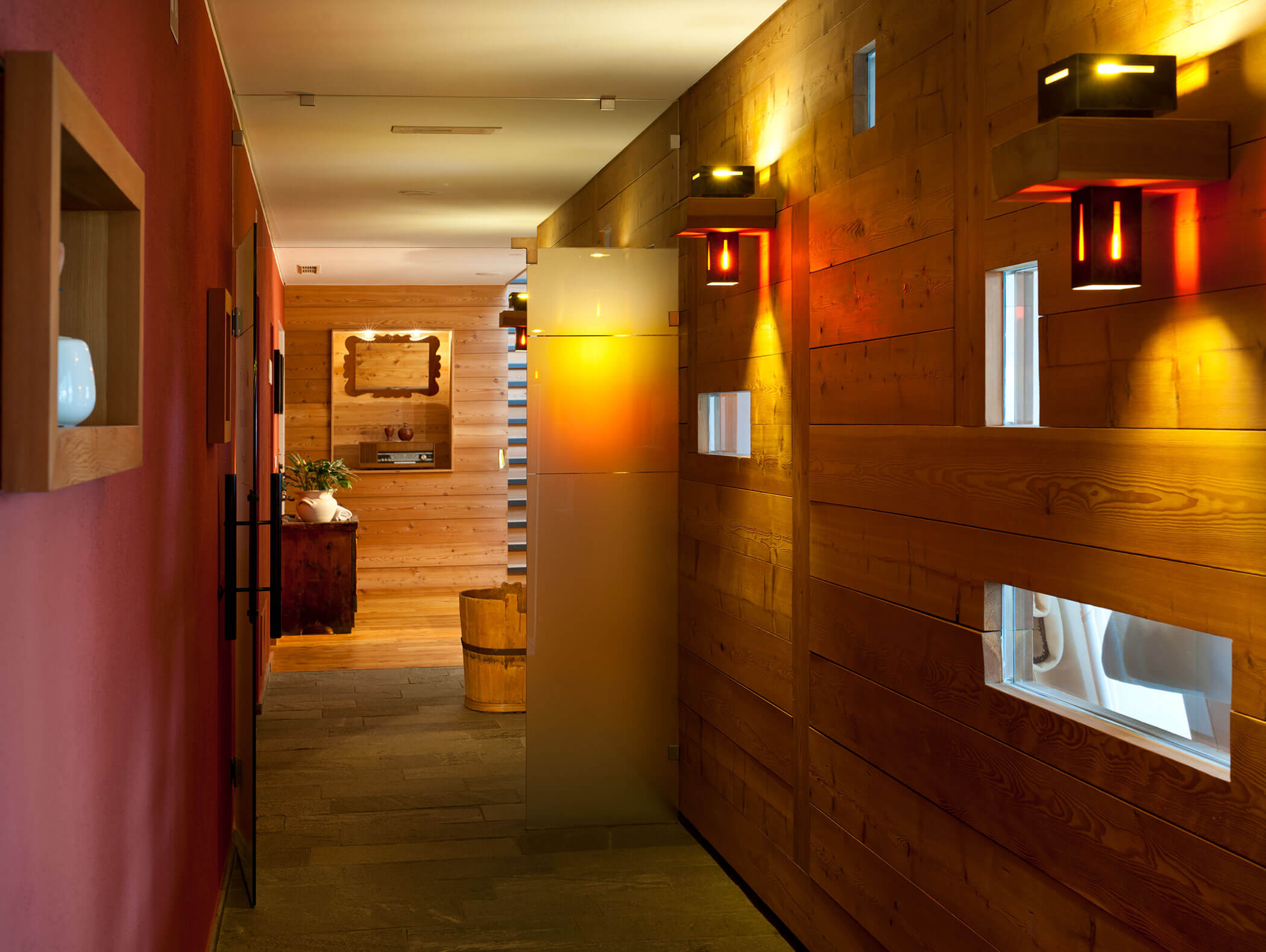Un accogliente corridoio con pareti in legno, illuminazione calda e piccole finestre che lasciano entrare la luce naturale. - Hotel Moosmair
