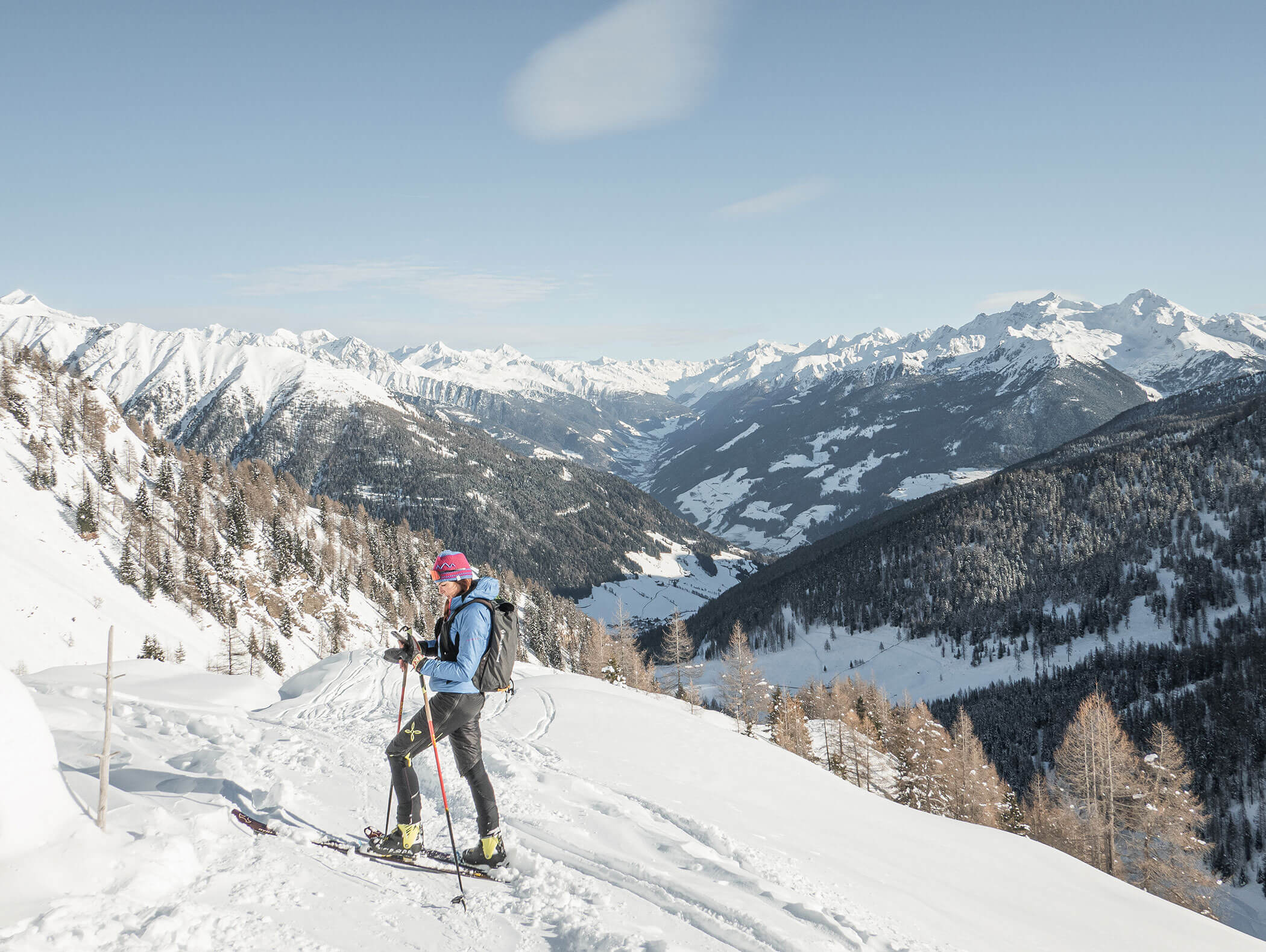 Uno sciatore si trova su un pendio di montagna innevato con cime e valli innevate sullo sfondo. - Hotel Moosmair