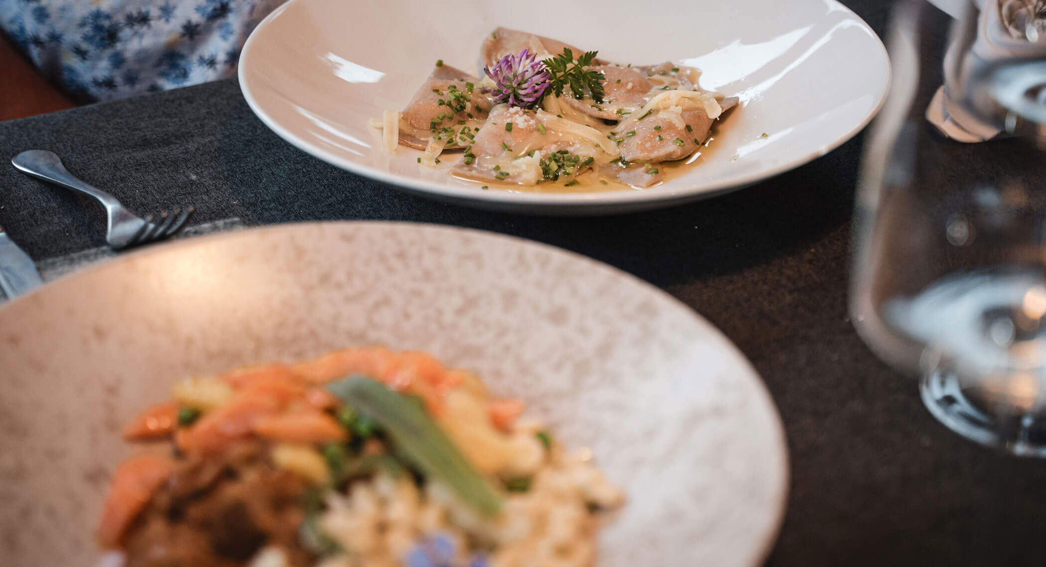 Two plated pasta dishes on a restaurant table, one with ravioli and the other with mixed vegetables. - Hotel Moosmair
